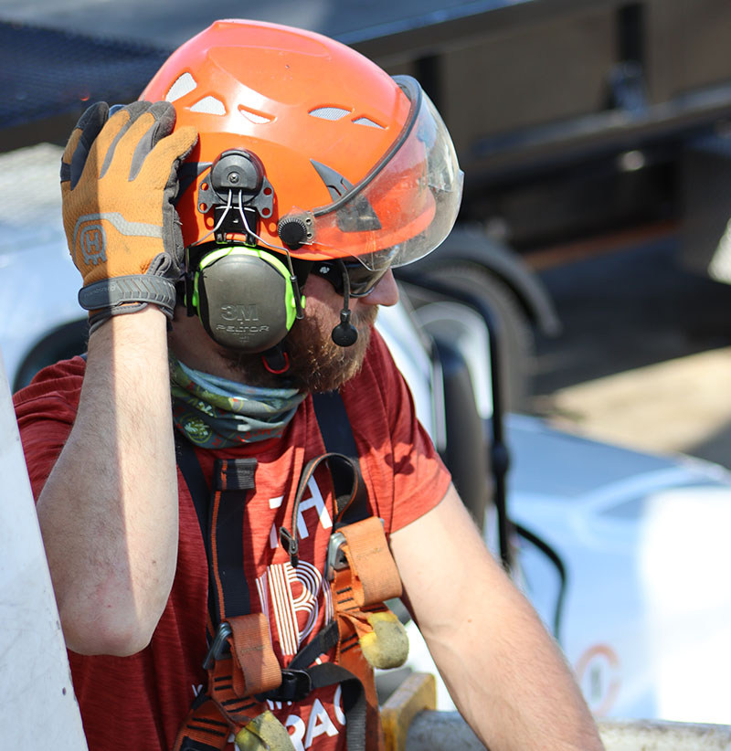 A tree care worker wearing a helmet, hearing protection and safety glasses preparing to operate a aerial lift.