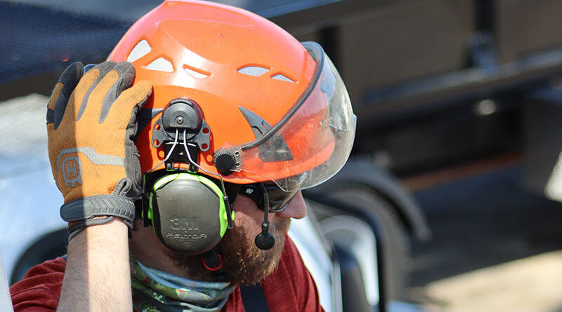 A tree care worker wearing a helmet, hearing protection and safety glasses preparing to operate a aerial lift.